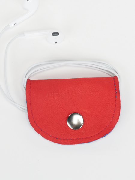 Red and royal blue Bèl Mizik Earbud Holder with snap closure. Front view showing the closed red exterior with earbuds wrapped around product.