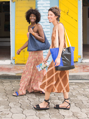 Royal Blue leather Caribbean Tire Tote with inner tube front panel and bottom, natural leather straps, and wooden button closure by deux mains. Shot of two female models walking down the street. 