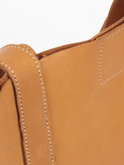 Tan leather Classic City Tote with inner tube bottom panel, and magnetic closure by deux mains. Close up showing contrast white stitching on handles and center closure. 