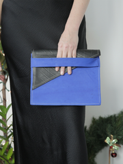 Royal blue leather City Classic Clutch, with diagonal black contrast fold-over by deux mains. Close up of female model holding clutch by her side. 