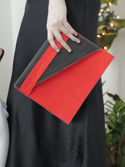 Red leather City Classic Clutch, with diagonal black contrast fold-over by deux mains. Close up of female model holding the clutch by her side. 