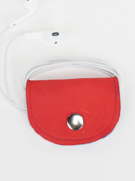 Red and royal blue Bèl Mizik Earbud Holder with snap closure. Front view showing the closed red exterior with earbuds wrapped around product. 