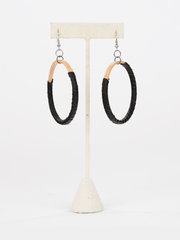 Black leather Hispaniola Hoop Earrings with individually crafted wooden circle centerpiece. View of earrings hung from earring holder. 
