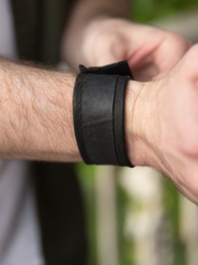 Black Leather and Tire Cuff featuring upcycled inner tube and snap closure. Close up of male model wearing the Leather and Tire Cuff on his wrist. 