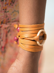 Tan leather Bonjou Wrap Bracelet with wooden ring center, and dark red ceramic beads. Close up shot of female model with bracelet around her wrist. 